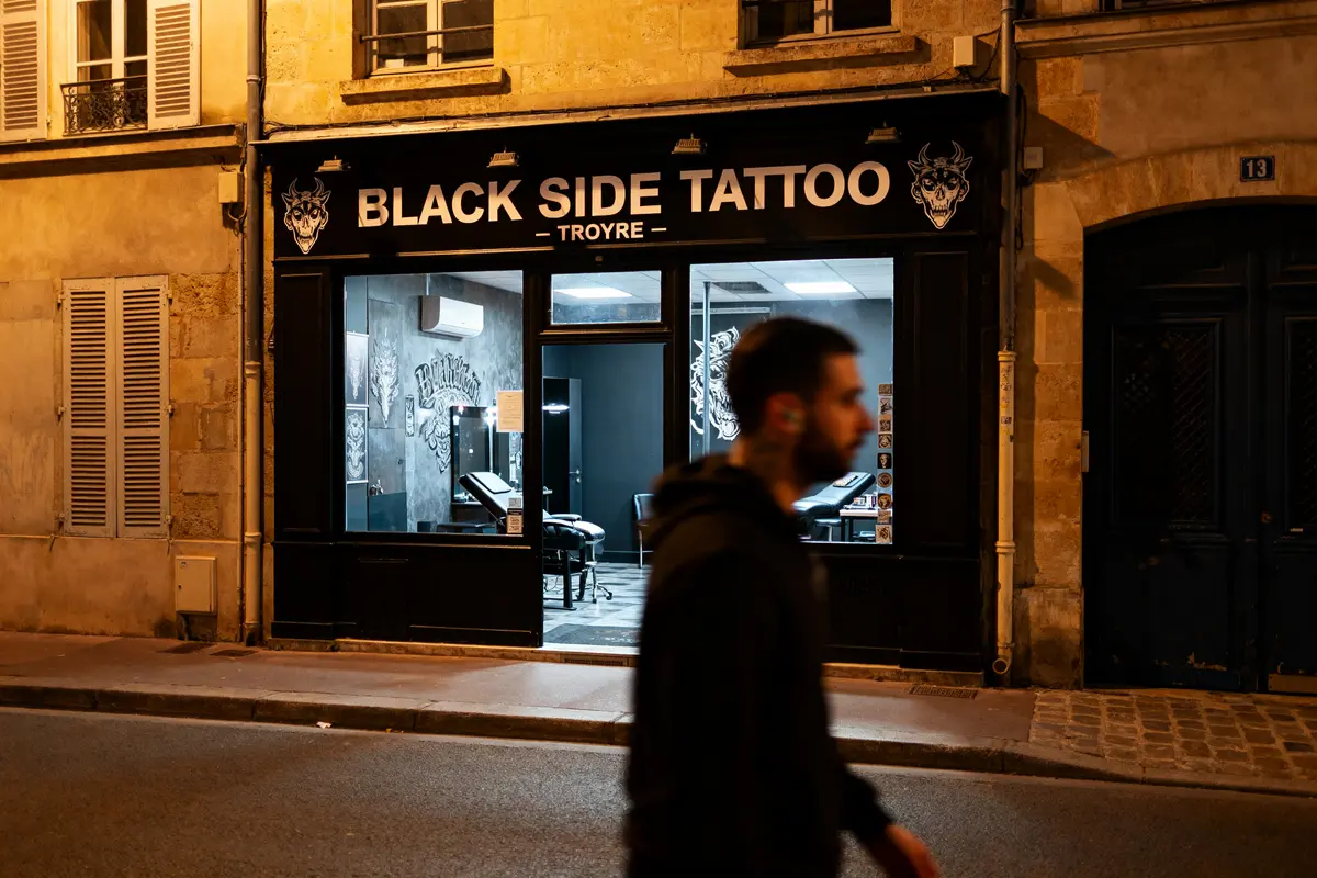Façade du magasin Black Side Tattoo Troyes avec homme passant en soirée éclairée.