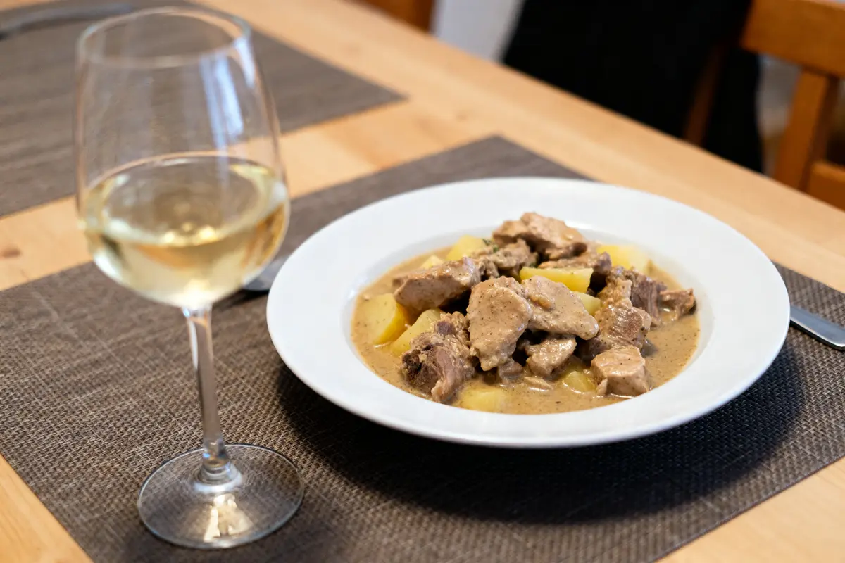 Verre de vin blanc accompagné d'une blanquette de veau savoureuse sur table en bois