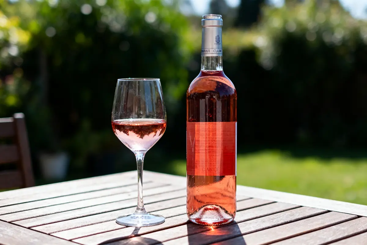 Bouteille et verre de vin rosé sur table en bois, jardin en arrière-plan.
