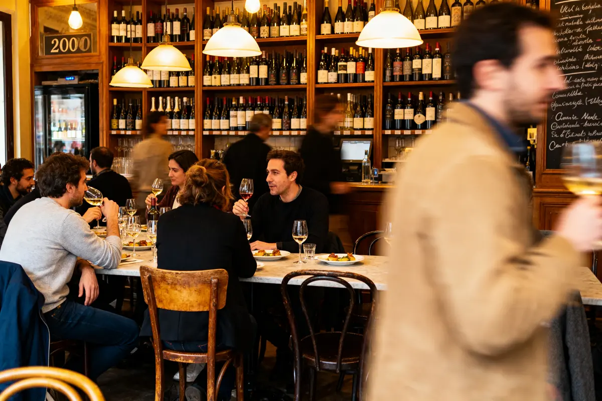 Personnes dînant dans un restaurant, dégustant du vin, avec des bouteilles de vin en arrière-plan.