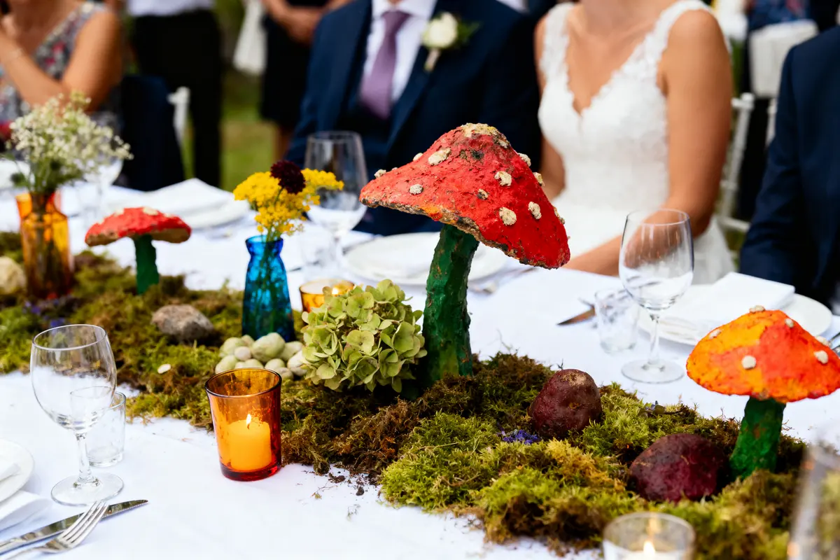 Déco de table avec champignons, mousse, fleurs, et bougies lors d'un événement en extérieur.