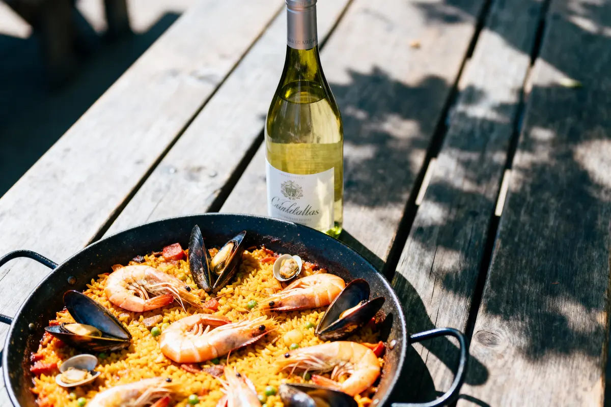 Paella aux fruits de mer avec crevettes, moules et bouteille de vin blanc sur table en bois.